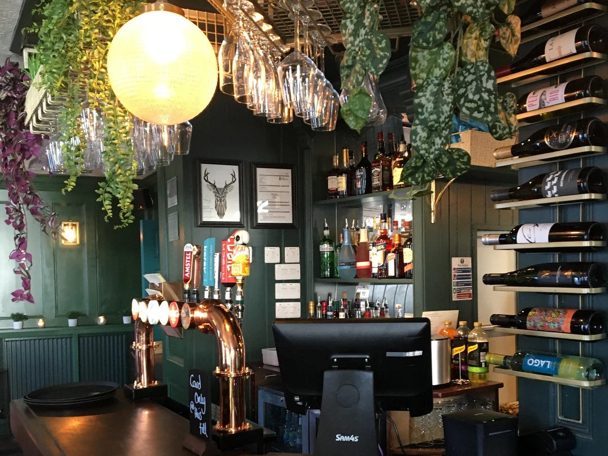 commercial-interior-pub-wooden-panelling-wallpaper-swansea-daffodil-decor-3 Bar with dark green painted panelling, shelves of bottles and hanging glasses