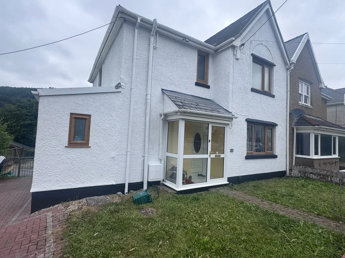 White rendered house with a bay window and a black painted plinth