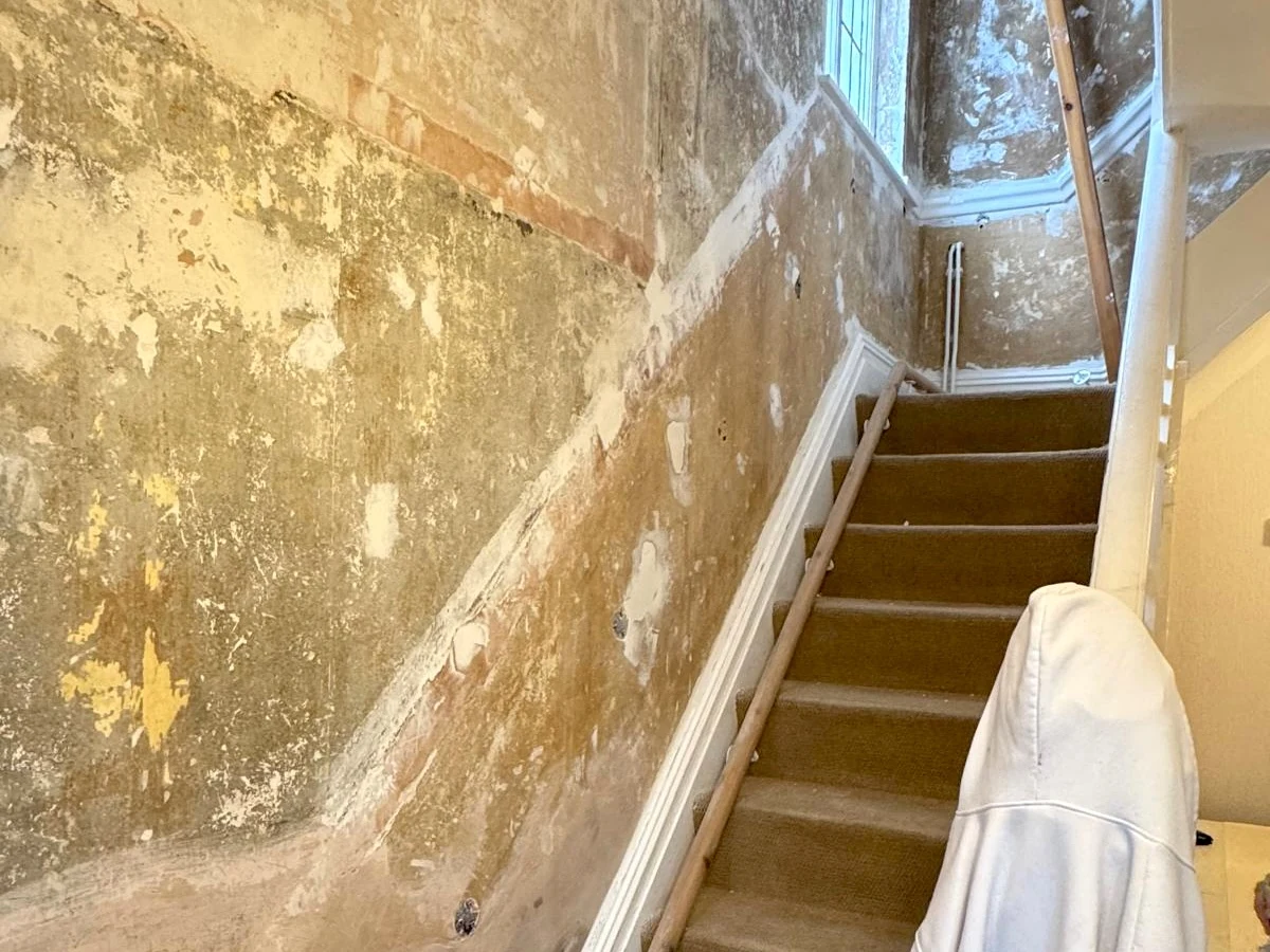 Hallway wall with old paint peeling off beside a staircase