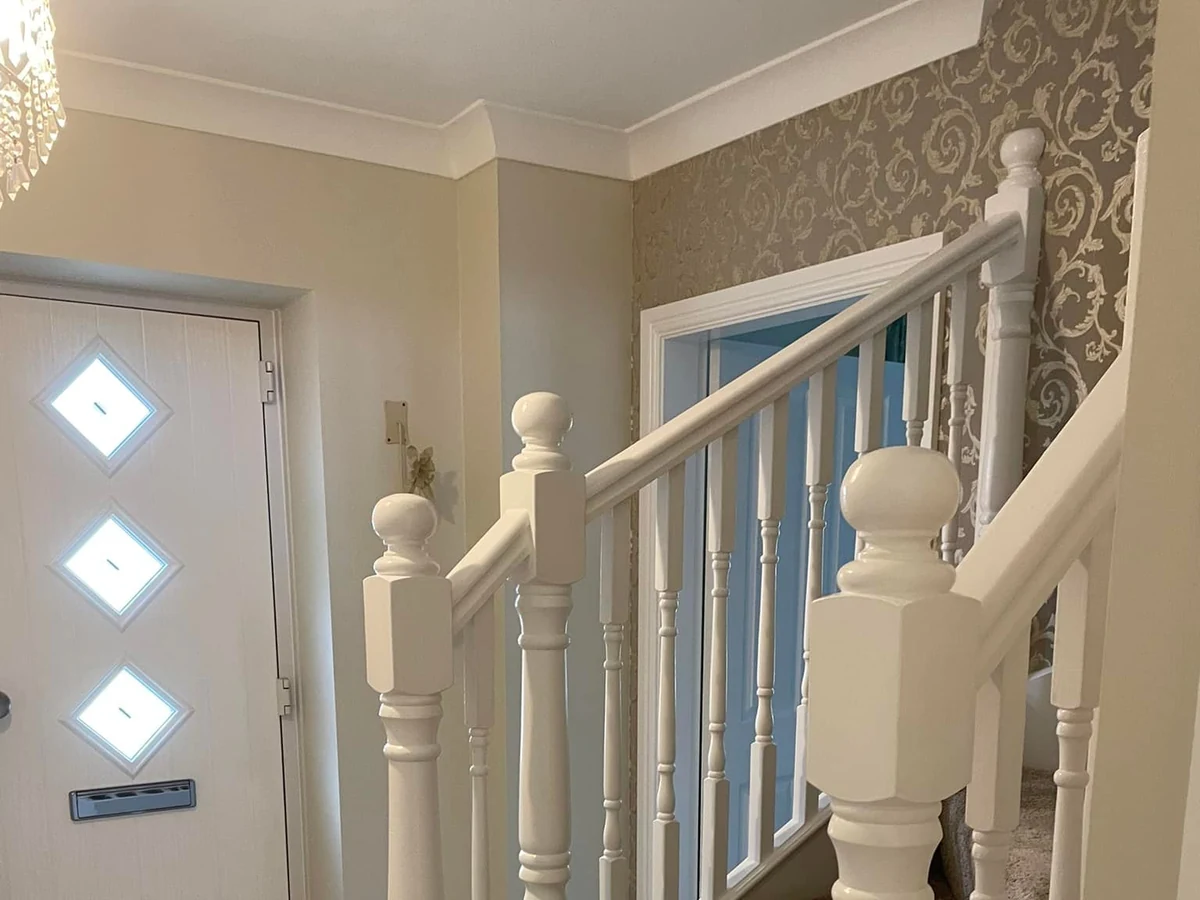 Hallway with wallpapered landing and painted white banisters in Loughor by Daffodil Decor